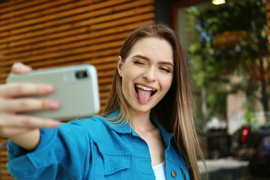Happy young woman taking selfie on city street