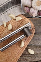 Garlic press and cloves on wooden table, top view