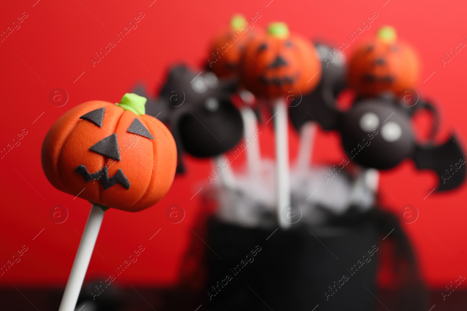 Photo of Delicious Halloween themed cake pops on red background, closeup. Space for text