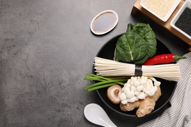 Photo of Cooking delicious ramen soup. Different ingredients in bowls and spoon on gray table, flat lay. Space for text