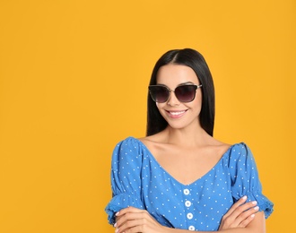 Beautiful woman wearing sunglasses on yellow background. Space for text