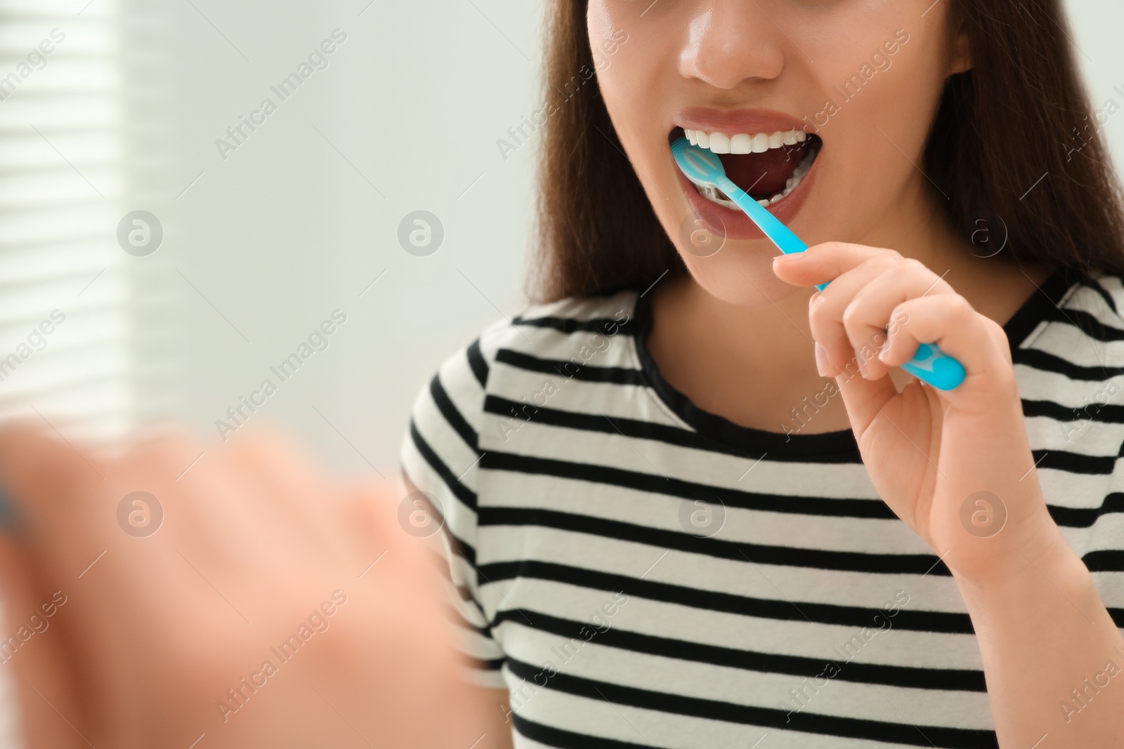 Photo of Woman brushing her teeth with plastic toothbrush near mirror in bathroom, closeup