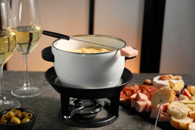 Photo of Forks with pieces of ham, bread and fondue pot with melted cheese on grey table, closeup