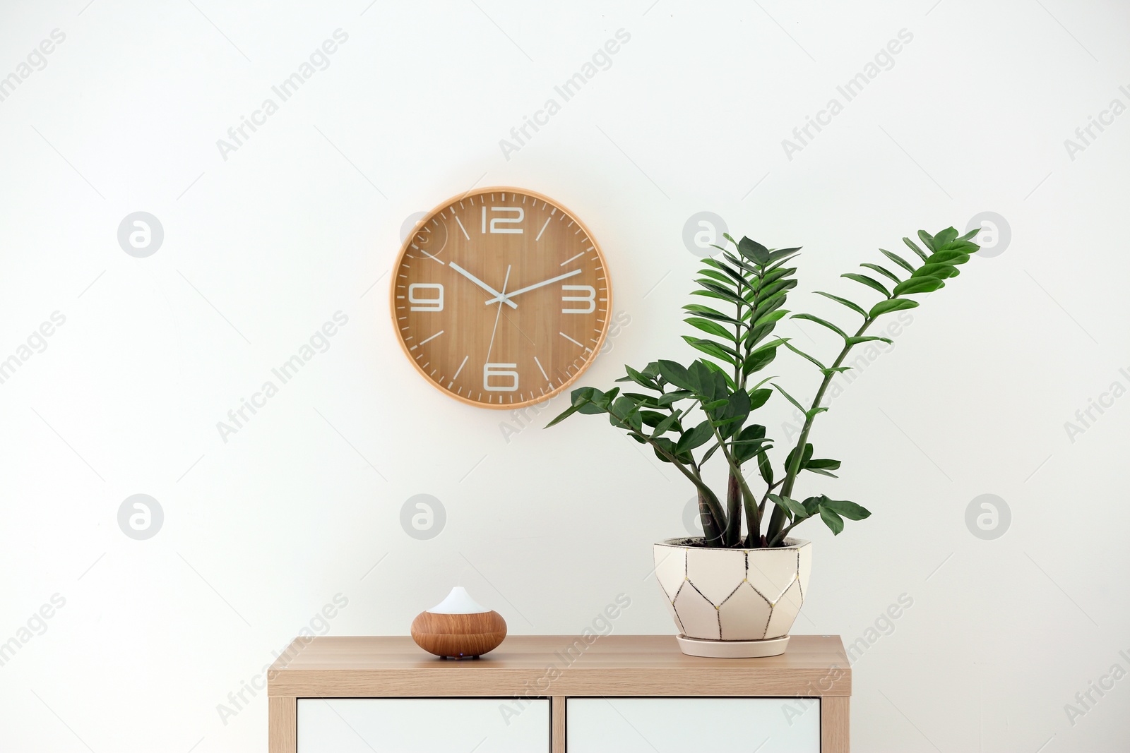 Photo of Aroma oil diffuser lamp and plant on cabinet against white wall