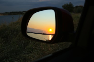 Reflection of landscape with beautiful sunset over calm river in car side view mirror, closeup