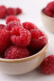 Photo of Tasty ripe raspberries in bowl on white table, closeup