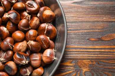 Photo of Delicious roasted edible chestnuts in frying pan on wooden table, top view. Space for text