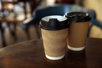 Photo of Cardboard takeaway coffee cups with plastic lids on wooden table in cafe, space for text