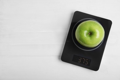 Photo of Ripe green apple and electronic scales on white wooden table, top view. Space for text