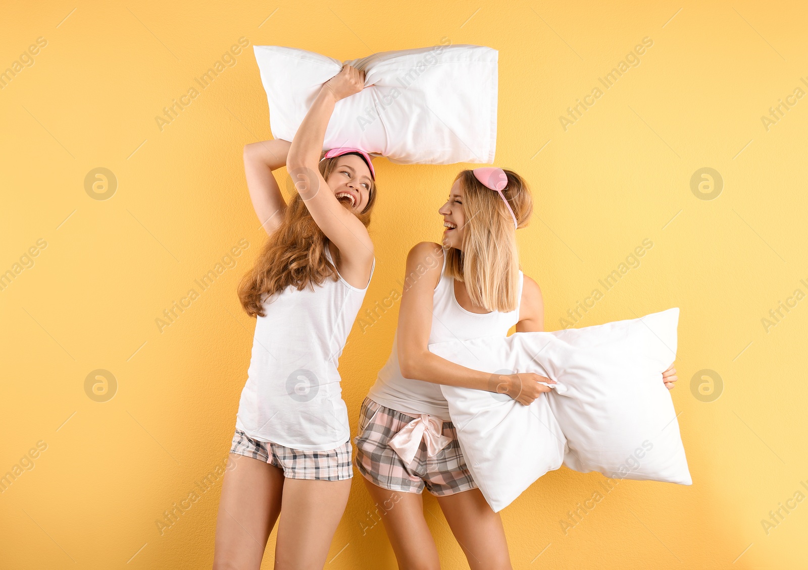 Photo of Two young women having pillow fight against color background