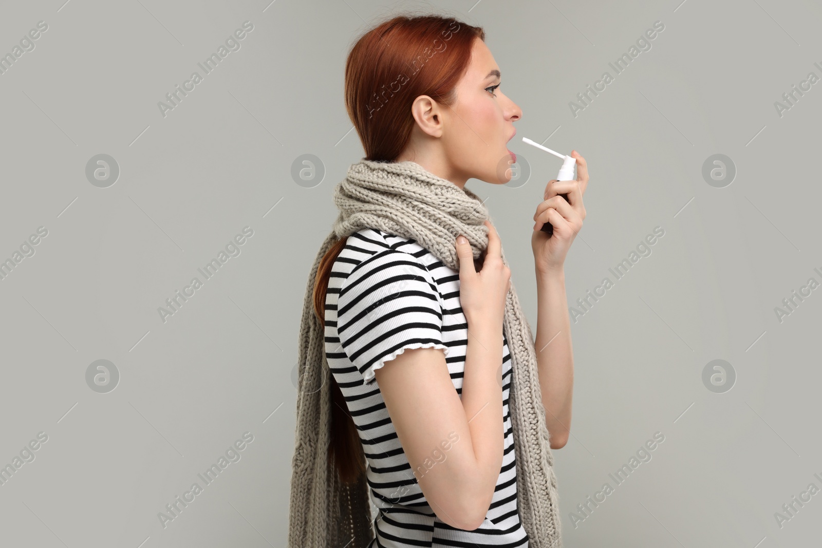 Photo of Young woman with scarf using throat spray on grey background