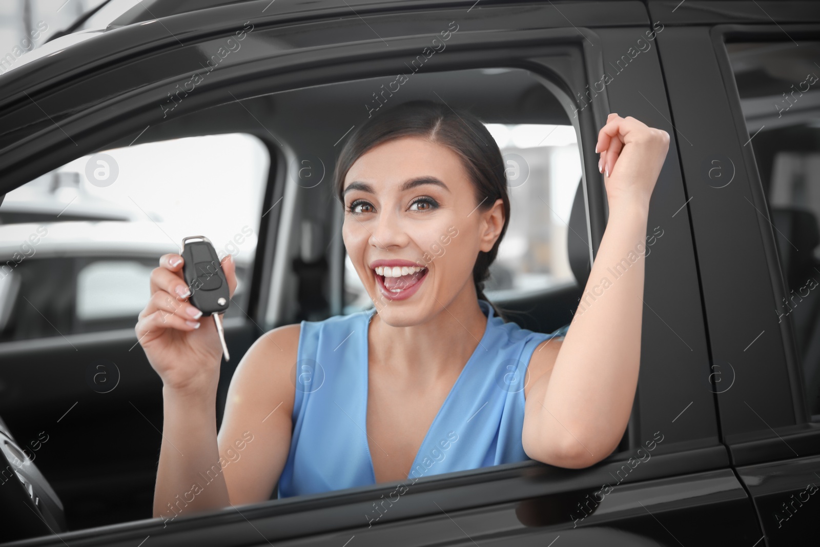 Photo of Young woman with key sitting in driver's seat of new car at salon