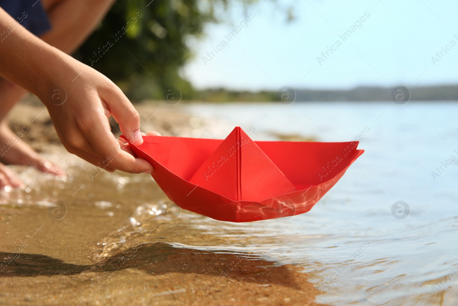 Photo of Little child playing with paper boat near river, closeup