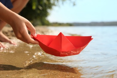 Little child playing with paper boat near river, closeup
