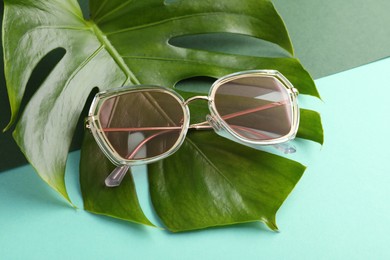 Photo of Stylish sunglasses and tropical leaf on color background, closeup