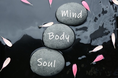 Image of Stones with words Mind, Body, Soul and flower petals in water, flat lay. Zen lifestyle