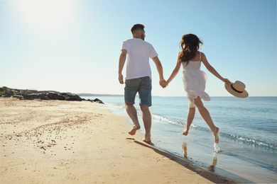 Photo of Young couple running on beach near sea. Honeymoon trip