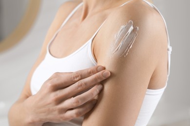 Woman applying body cream onto arm indoors, closeup