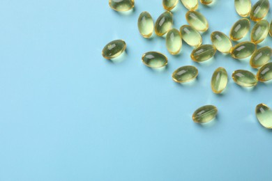 Photo of Vitamin capsules on light blue background, top view. Space for text