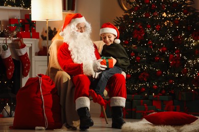 Photo of Merry Christmas. Little boy taking gift from Santa Claus in room