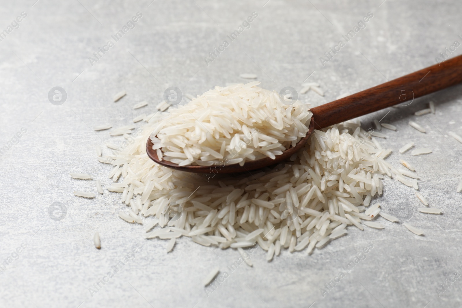 Photo of Raw basmati rice and wooden spoon on grey table