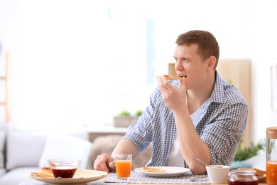 Photo of Young man eating tasty toasted bread with jam at table