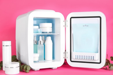 Photo of Open cosmetic refrigerator and skin care products on pink background