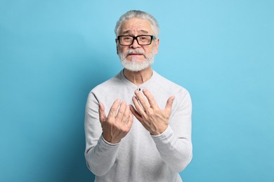 Arthritis symptoms. Man suffering from pain in hands on light blue background