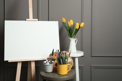 Easel with blank canvas, brushes, paints and palette in studio