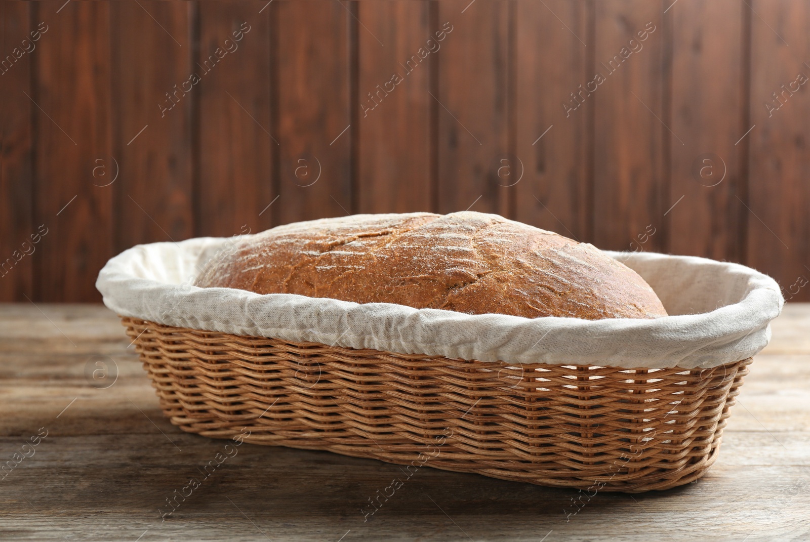 Photo of Loaf of tasty fresh bread in wicker basket on wooden table