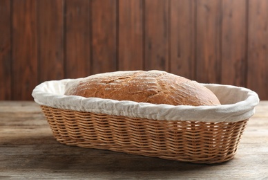 Photo of Loaf of tasty fresh bread in wicker basket on wooden table