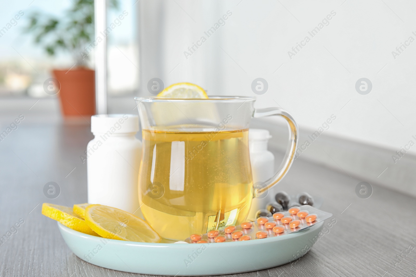 Photo of Jug of hot tea with lemon and cold remedies on wooden table