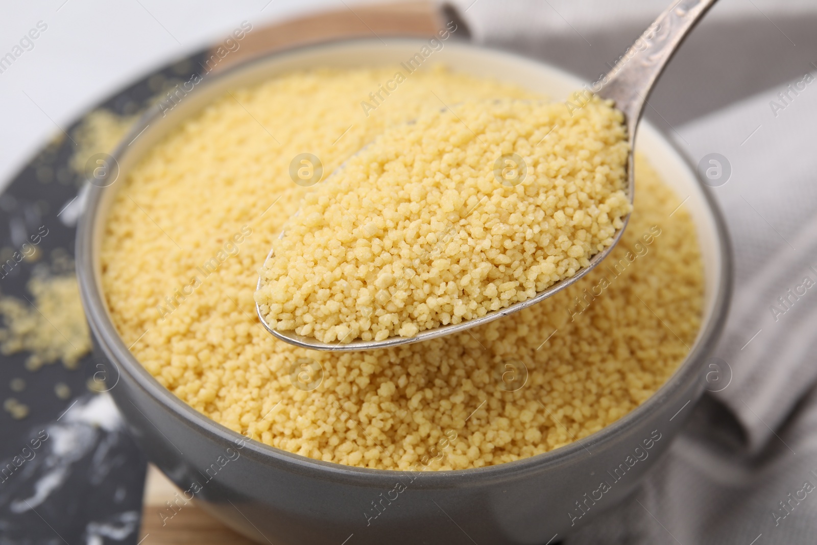 Photo of Taking raw couscous with spoon from bowl, closeup