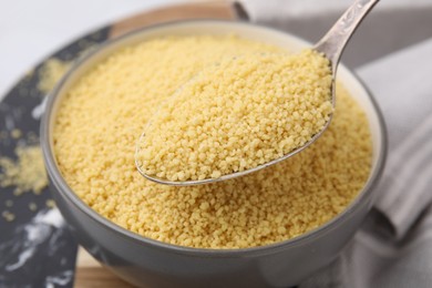 Photo of Taking raw couscous with spoon from bowl, closeup