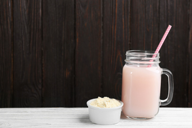 Protein shake and powder on white wooden table, space for text