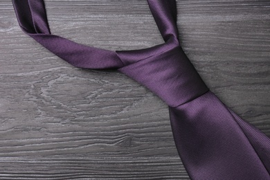 Stylish purple silk necktie on dark grey wooden table, top view