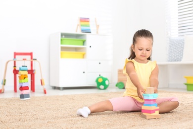 Cute little girl playing with toy on floor at home, space for text