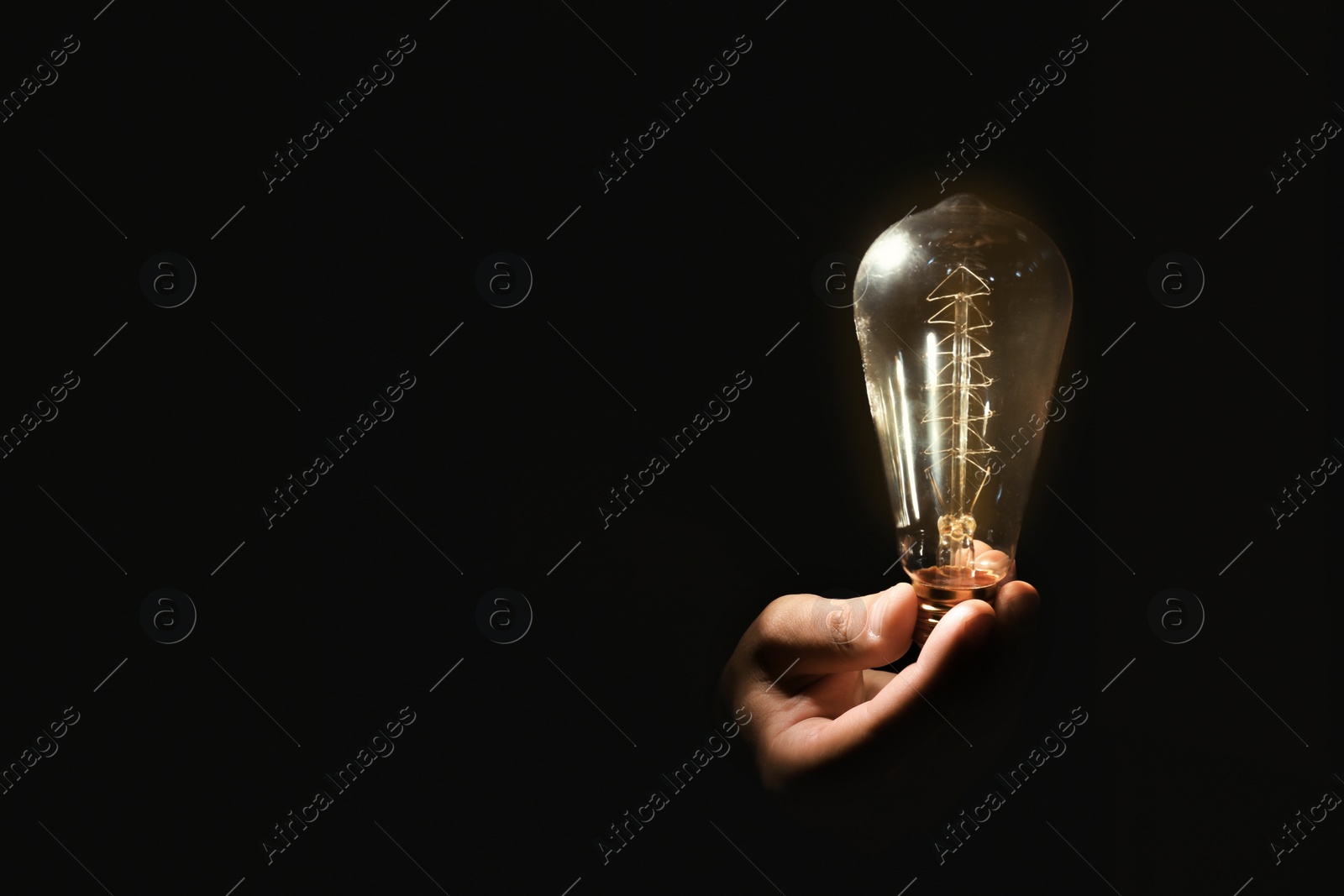 Photo of Man holding modern lamp bulb on dark background, closeup. Space for text