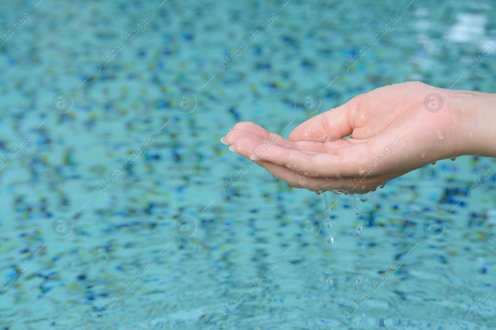 Photo of Girl holding water in hand above pool, closeup. Space for text