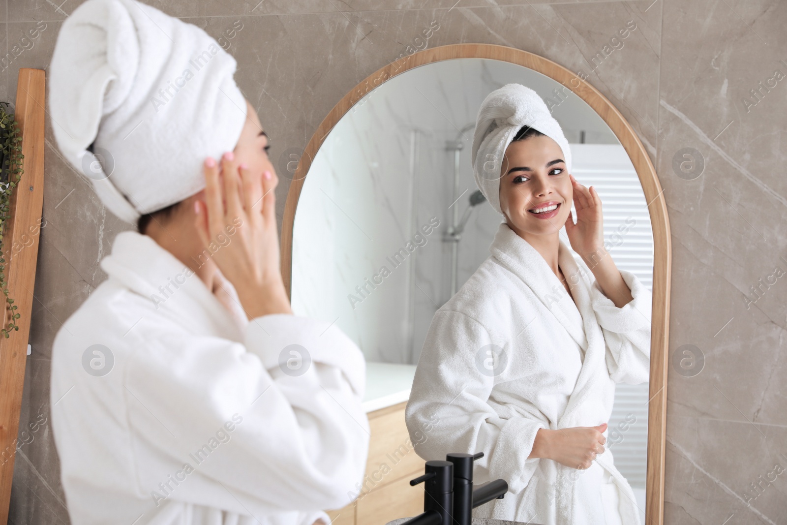 Photo of Beautiful young woman looking at herself in bathroom mirror