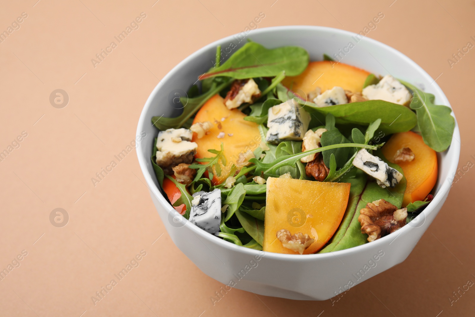 Photo of Tasty salad with persimmon, blue cheese and walnuts served on light brown background, space for text
