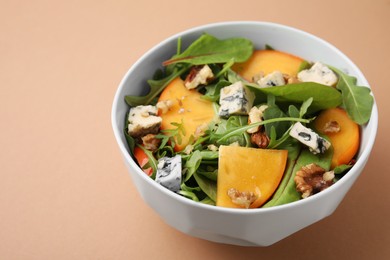 Tasty salad with persimmon, blue cheese and walnuts served on light brown background, space for text