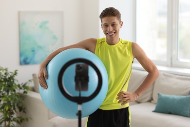 Photo of Smiling sports blogger holding fit ball while streaming online fitness lesson at home