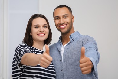 Dating agency. Happy couple showing thumbs up near white wall