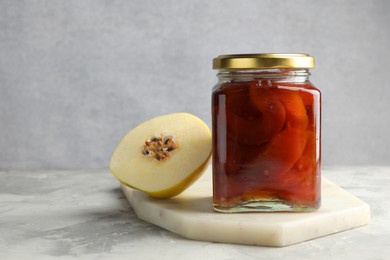 Photo of Tasty homemade quince jam in jar and half of fruit on grey textured table. Space for text
