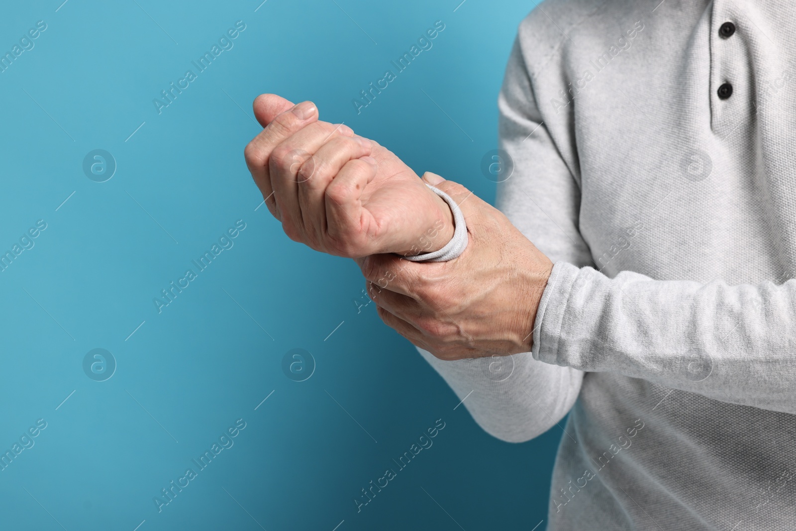 Photo of Arthritis symptoms. Man suffering from pain in wrist on light blue background, closeup. Space for text