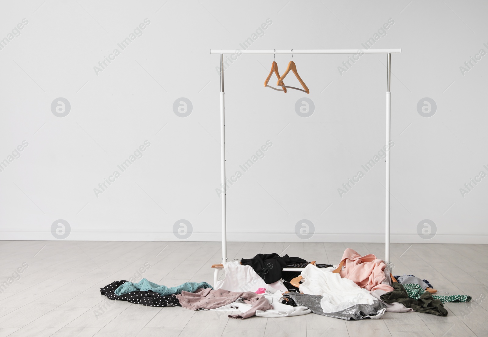 Photo of Wardrobe rack with hangers and pile of clothes on floor indoors. Space for text