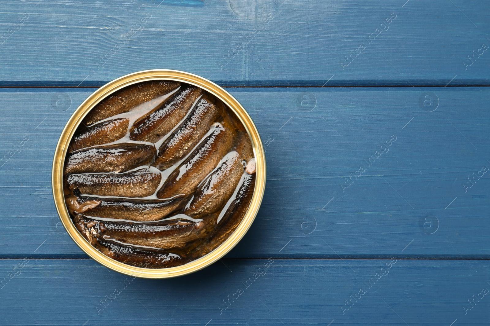 Photo of Open tin can of sprats on blue wooden table, top view. Space for text