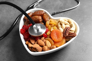 Photo of Heart shaped bowl with dried fruits, nuts and stethoscope on grey background