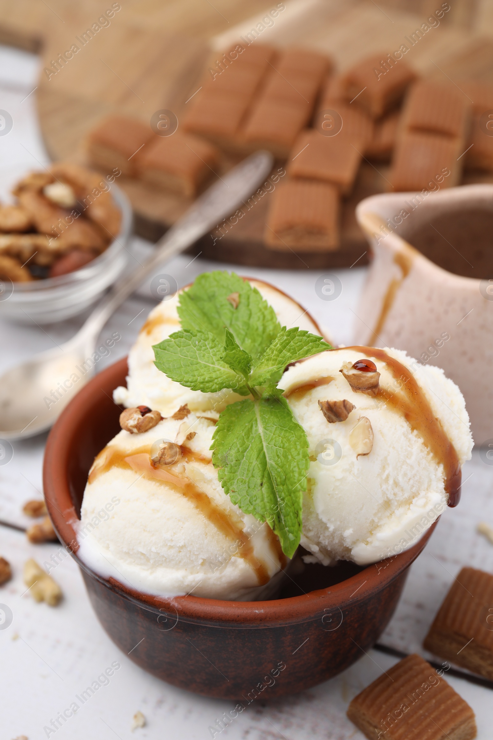 Photo of Bowl of tasty ice cream with caramel sauce, mint, nuts and candies on white table, closeup